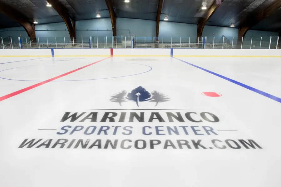 La pista recién preparada con el logotipo del Warinanco Sports Center en el centro del hielo, las líneas rojas y azules y las vigas curvas de madera del techo arriba. — Warinanco Sports Center
