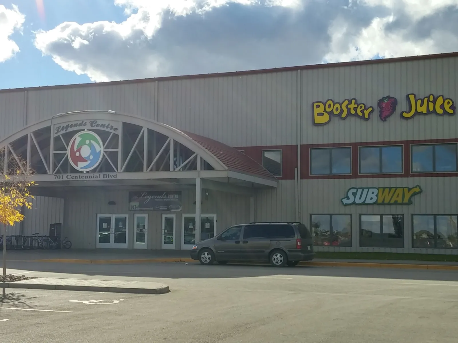 El frente del Warman Home Centre Communiplex, con su entrada de vidrio en arco y letreros de Booster Juice y Subway en la fachada. — Warman Home Centre Communiplex