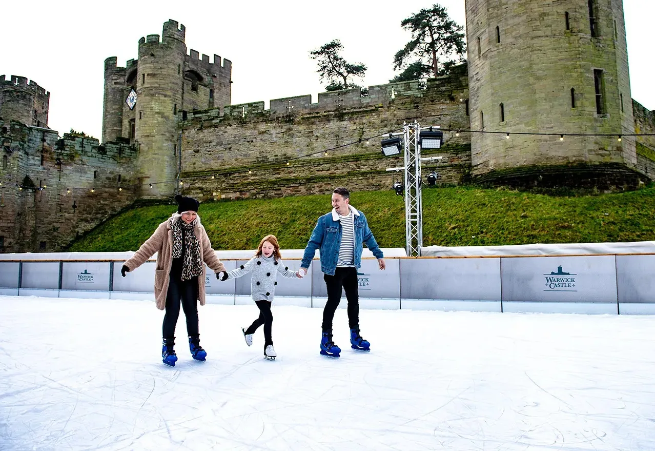 The open-air rink at Warwick Castle, skaters on the ice with the castle's stone wall and tower rising behind. — Warwick Castle Ice Rink