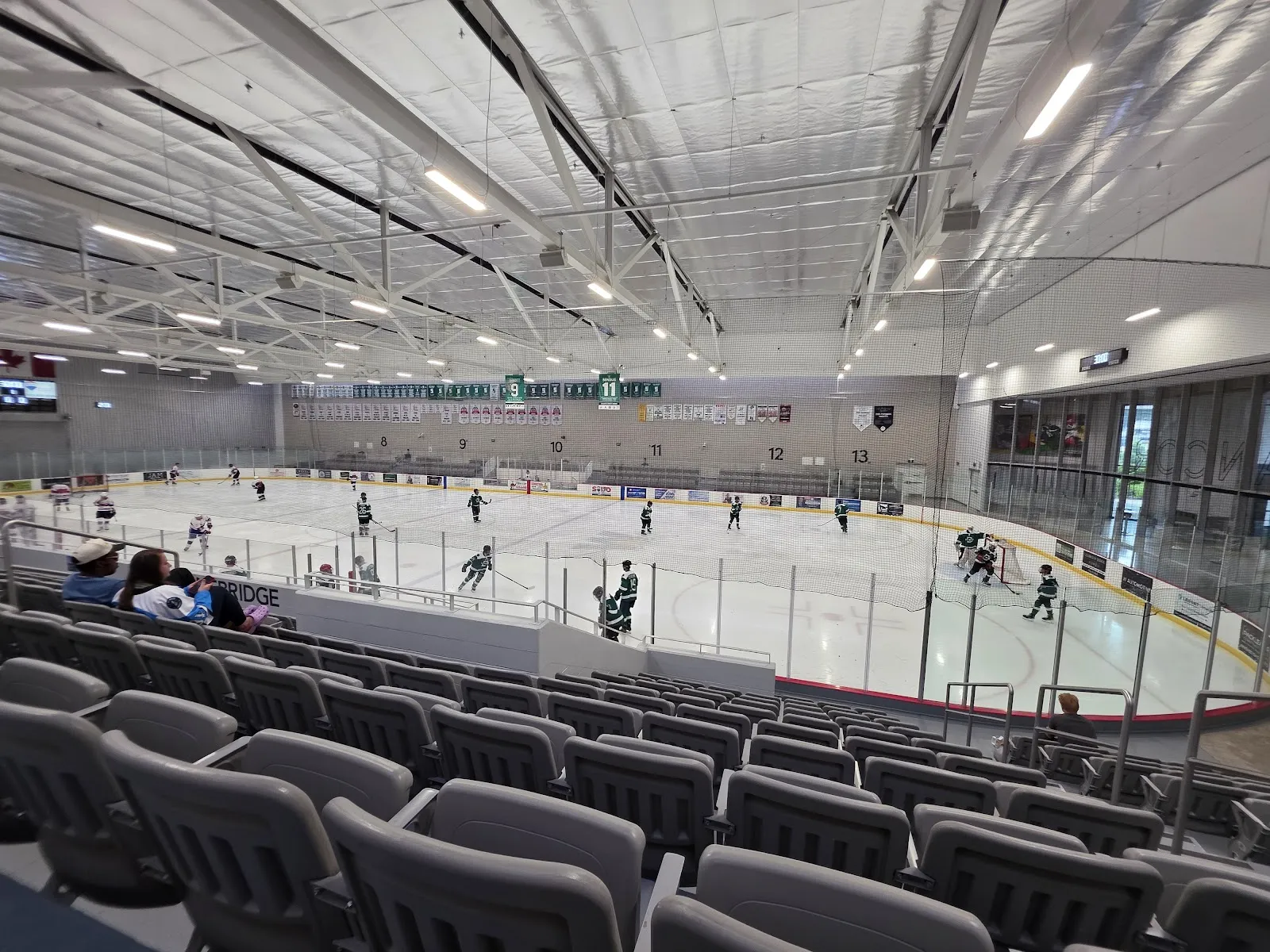 A rink from the grey stadium seats during a youth game, under the white roof. — Wasaga Stars Arena (Wasaga Beach)
