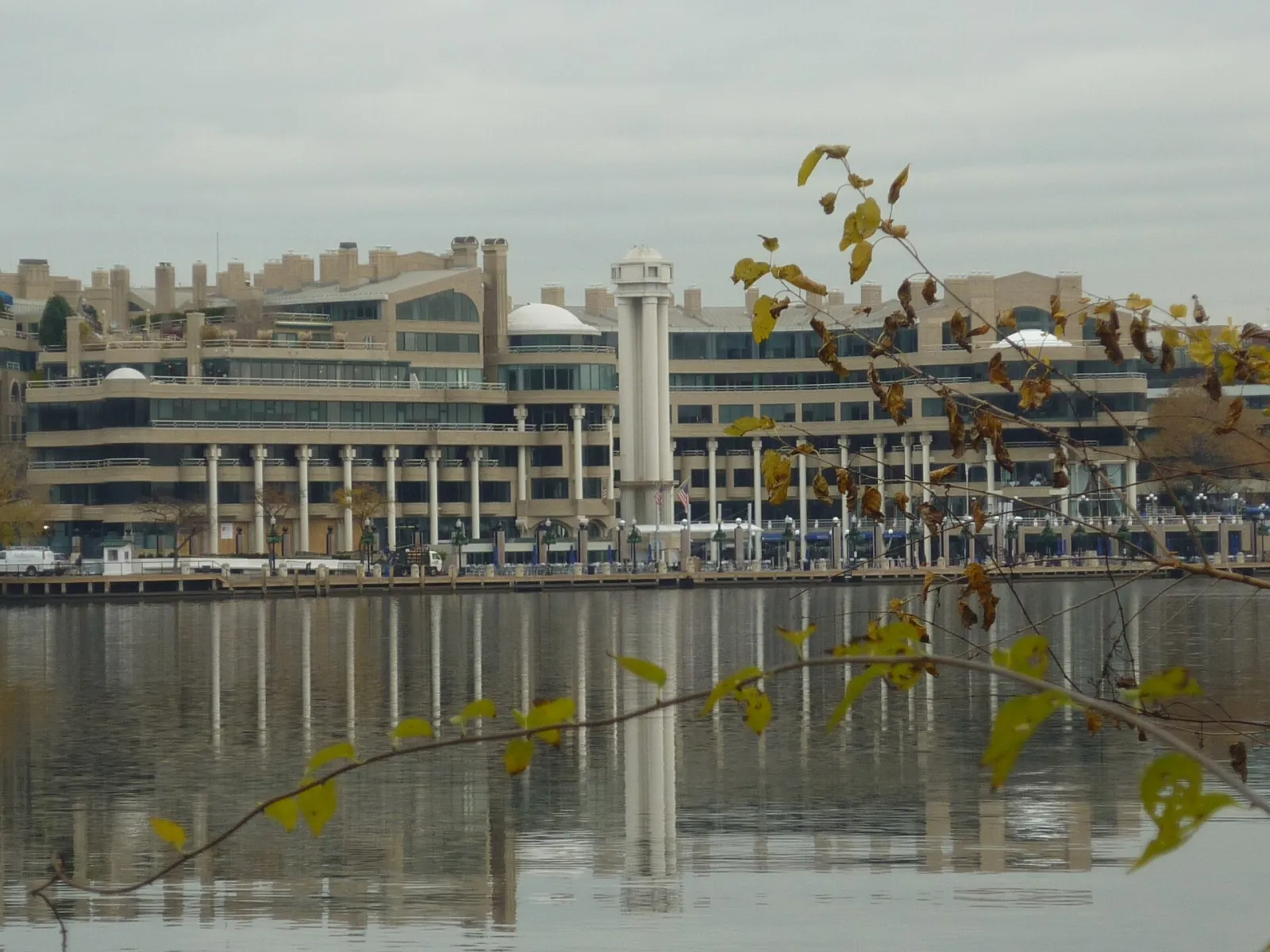 The Washington Harbour buildings on the Georgetown waterfront seen across the Potomac, with the white tower at the centre; the ice rink sits in the plaza at their foot — Washington Harbour Ice Rink