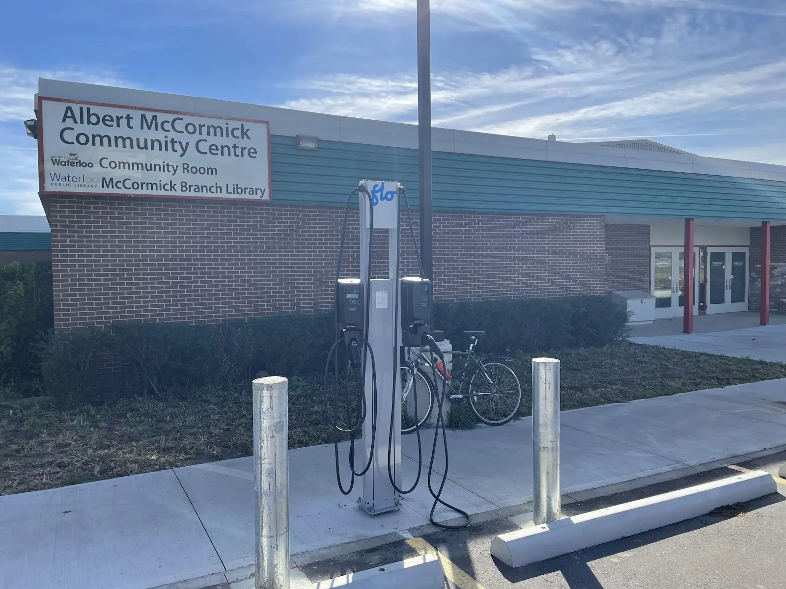 Muro de ladrillo del edificio con el letrero de "Albert McCormick Community Centre", portabicicletas y un cargador para vehículos eléctricos en la banqueta al frente. — Albert McCormick Community Centre