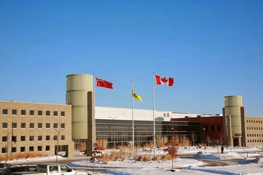 The RIM Park Manulife Sportsplex front in winter: long tan brick wings with round towers, three flagpoles and snow on the lawn. — RIM Park