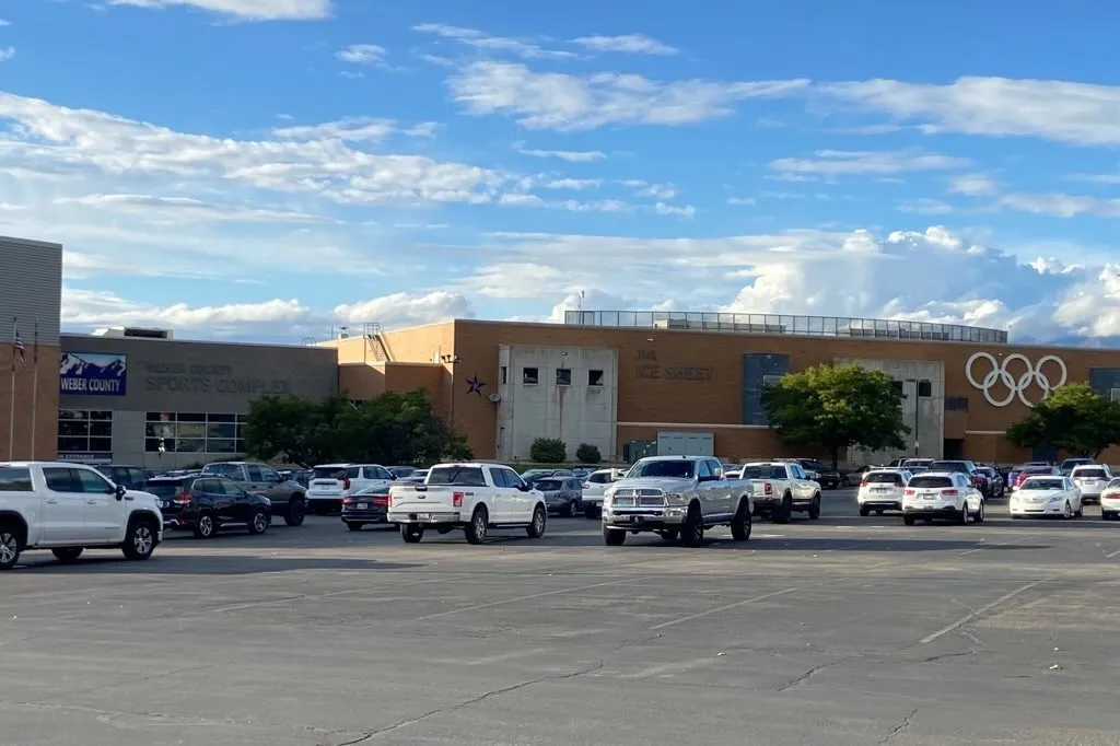 El Weber County Sports Complex de ladrillo visto desde su estacionamiento, con las letras 'The Ice Sheet' y los anillos olímpicos en el muro. — Weber County Ice Sheet