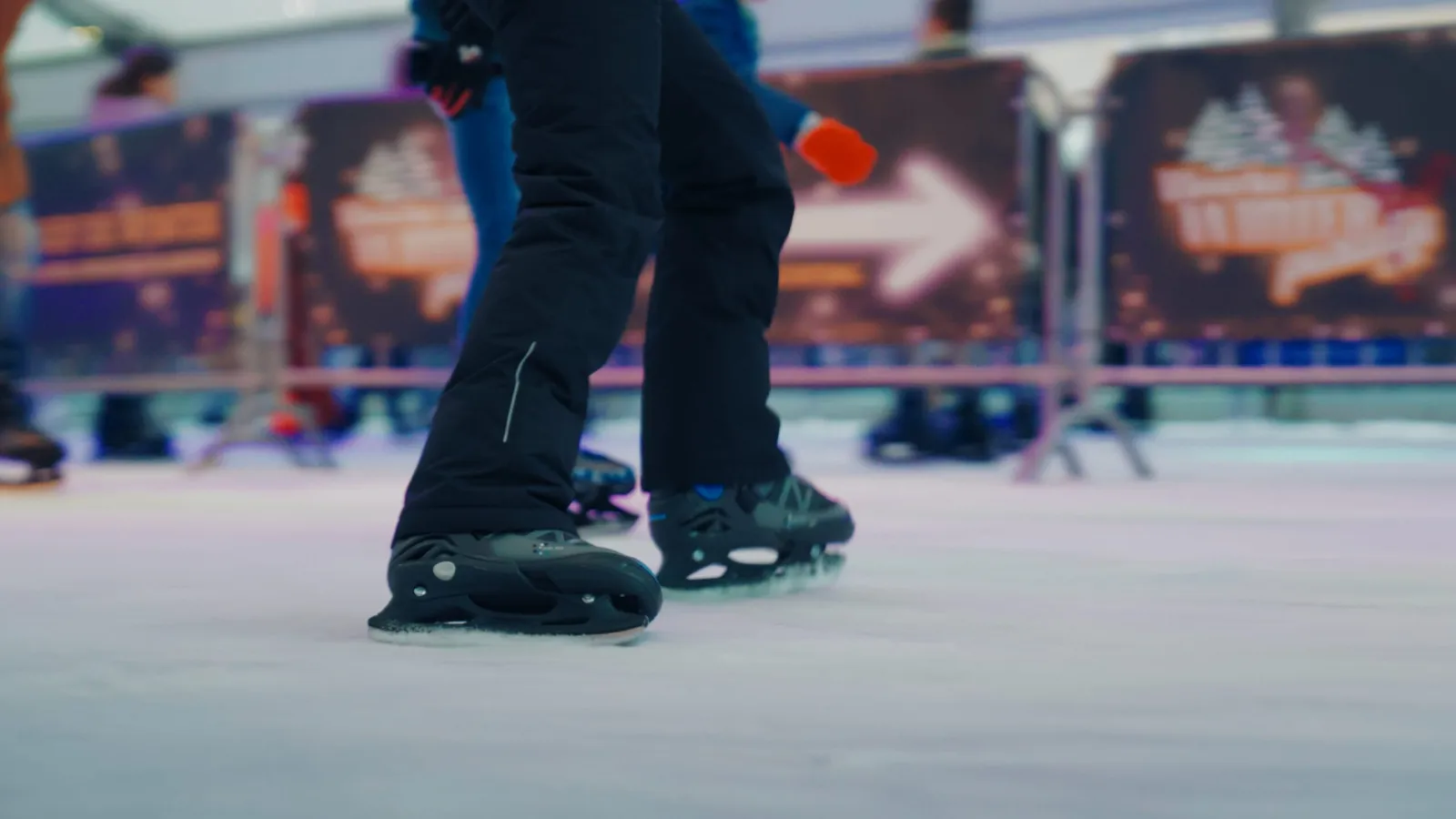 Schaatsen op de ijsbaan van echt ijs in het overdekte paviljoen, met de reclameborden op de achtergrond. – Weerter Winterparadijs