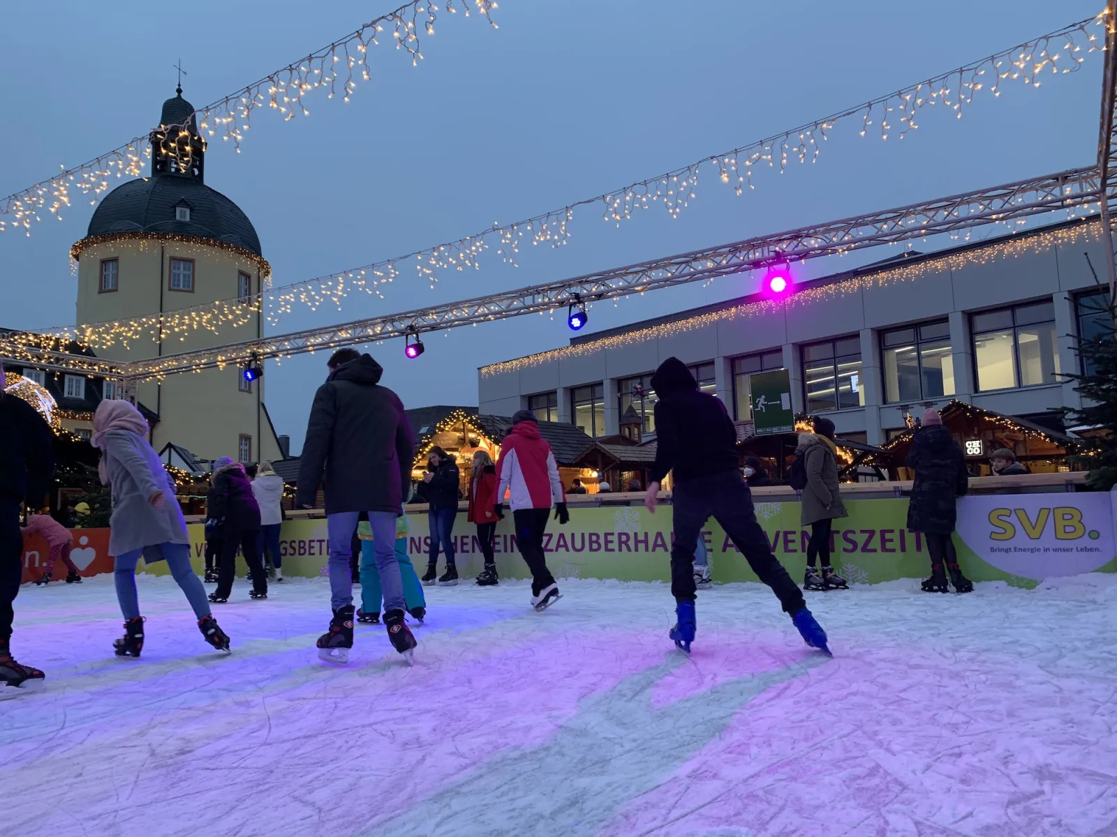 The Siegen Weihnachtsmarkt rink at dusk with lights strung overhead. — Eislaufbahn Weihnachtsmarkt Siegen