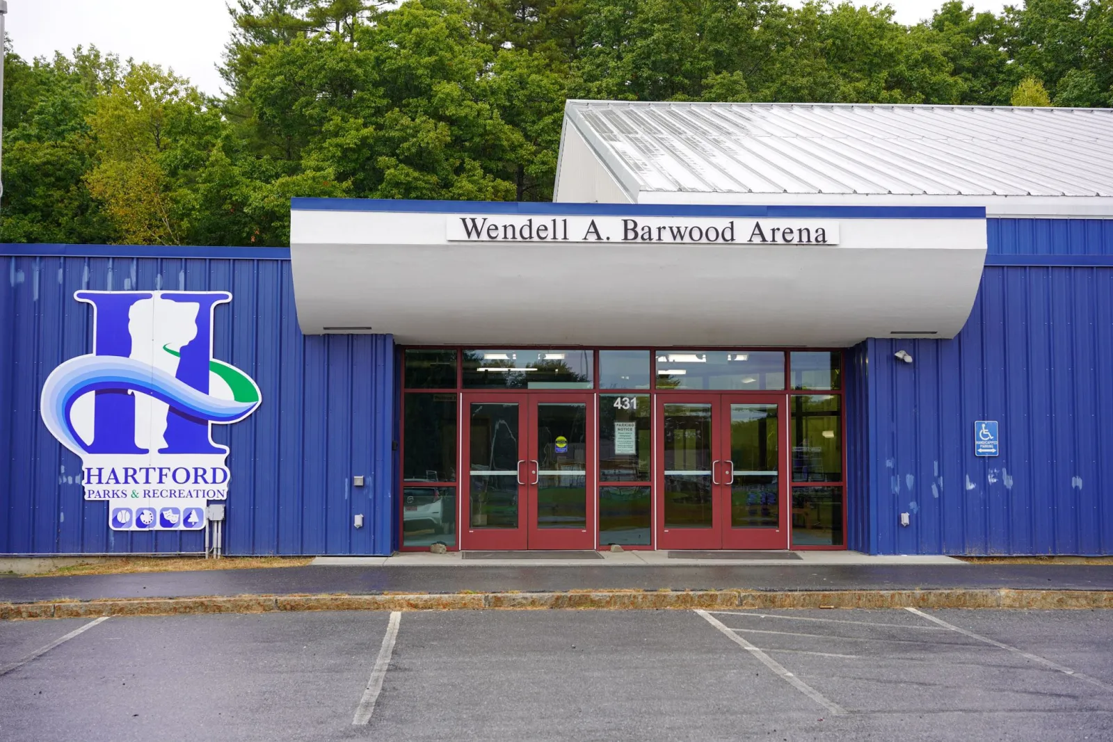 El frente azul revestido de metal de la arena, con una marquesina curva blanca que dice "Wendell A. Barwood Arena" sobre puertas rojas y el logotipo de Hartford Parks & Recreation. — Wendell A. Barwood Arena