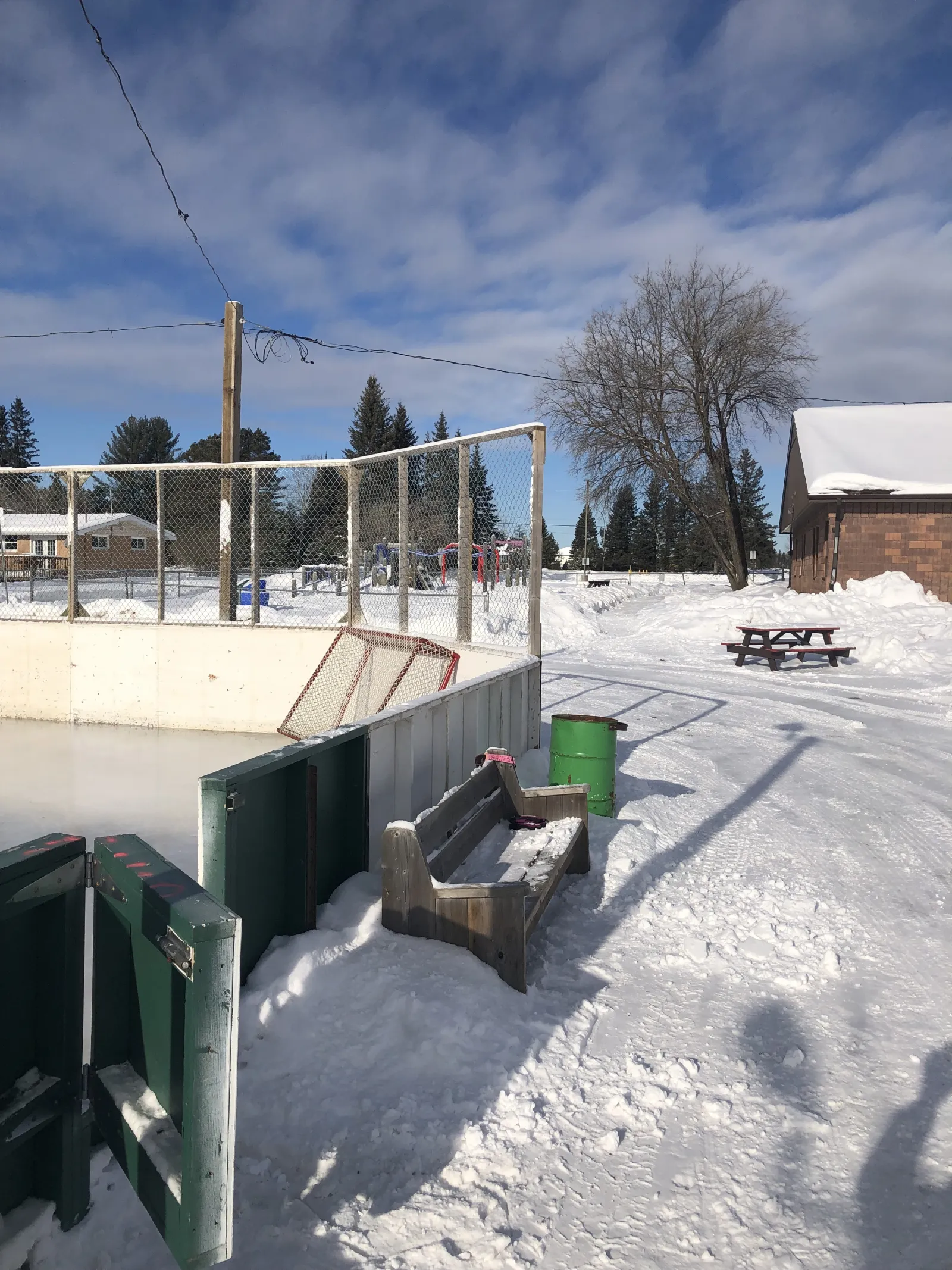 A bench, bin and picnic table beside the West Arthur Community Centre rink, with the building behind — West Arthur Community Centre Outdoor Rink