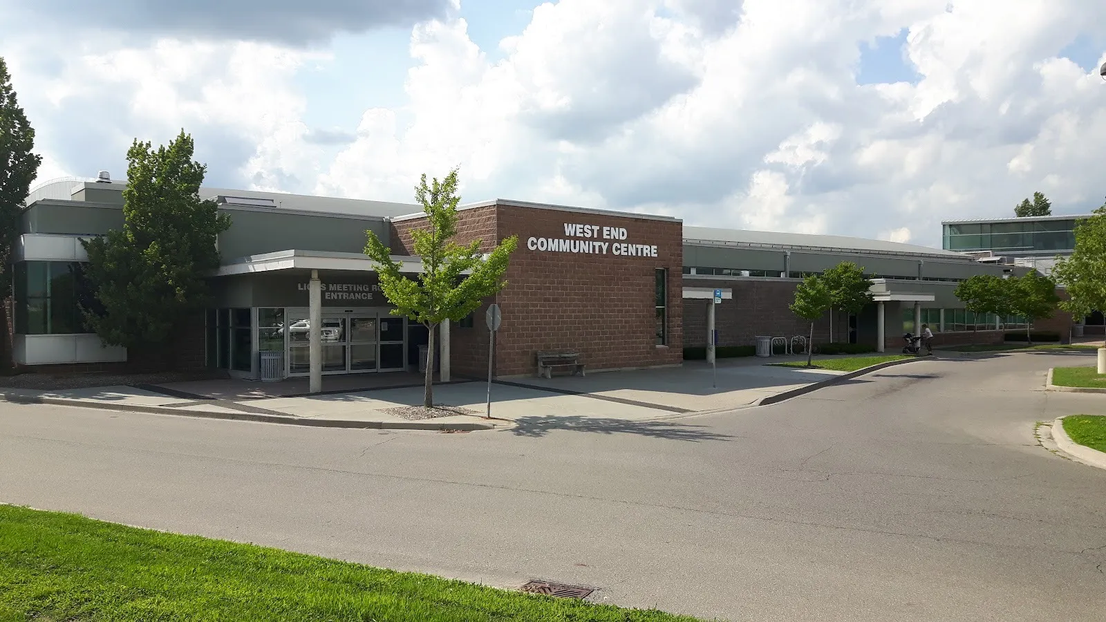 The West End Community Centre, its name on a brick tower beside the meeting-room entrance canopy, trees along the curved drive. — West End Community Centre (Guelph)