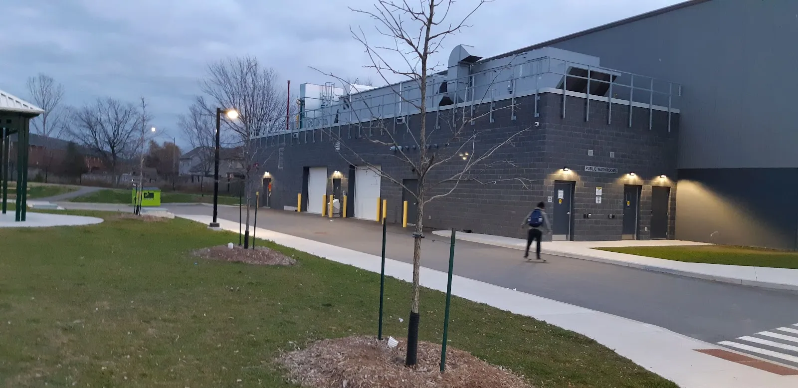 The grey and brick front of the West Lincoln Community Centre seen from the footpath, with young trees along the lawn. — West Lincoln Community Centre