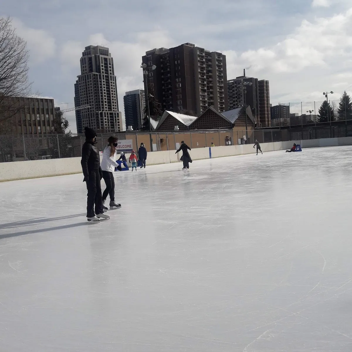 Patinadores en la pista al aire libre de West Mall en un luminoso día de invierno, con torres de departamentos detrás de la cerca — West Mall Rink Outdoor Ice Rinks