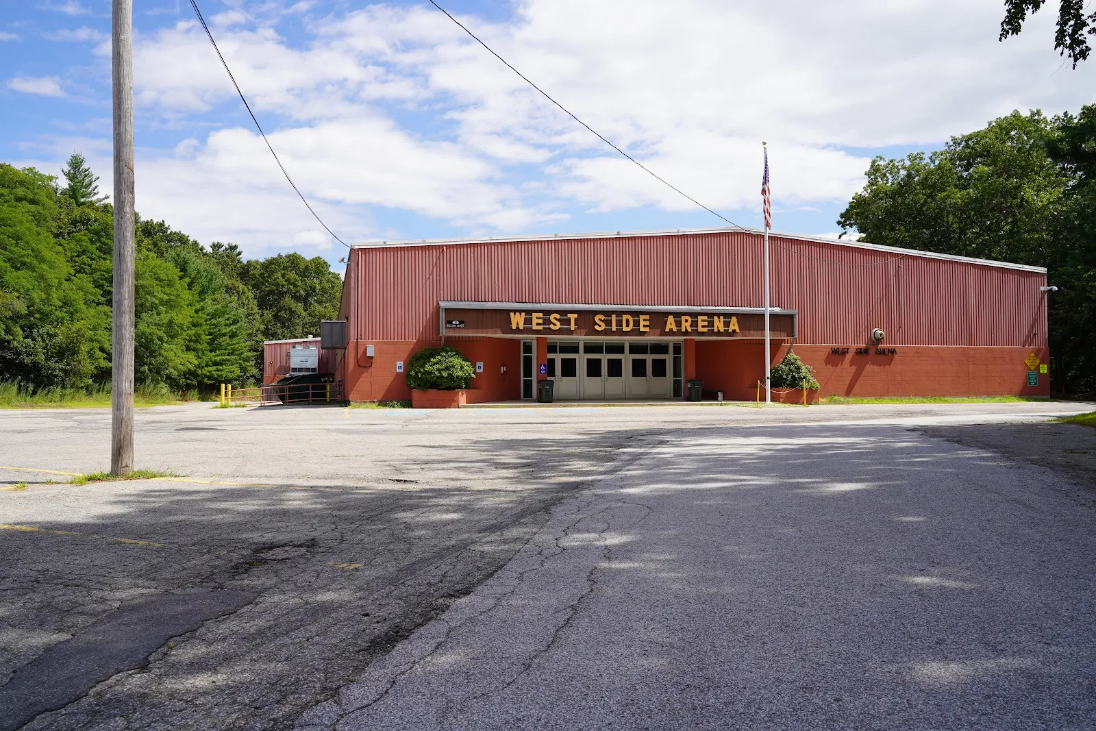 The arena's red metal building with the West Side Arena sign over the entrance, seen across the parking lot. — West Side Arena