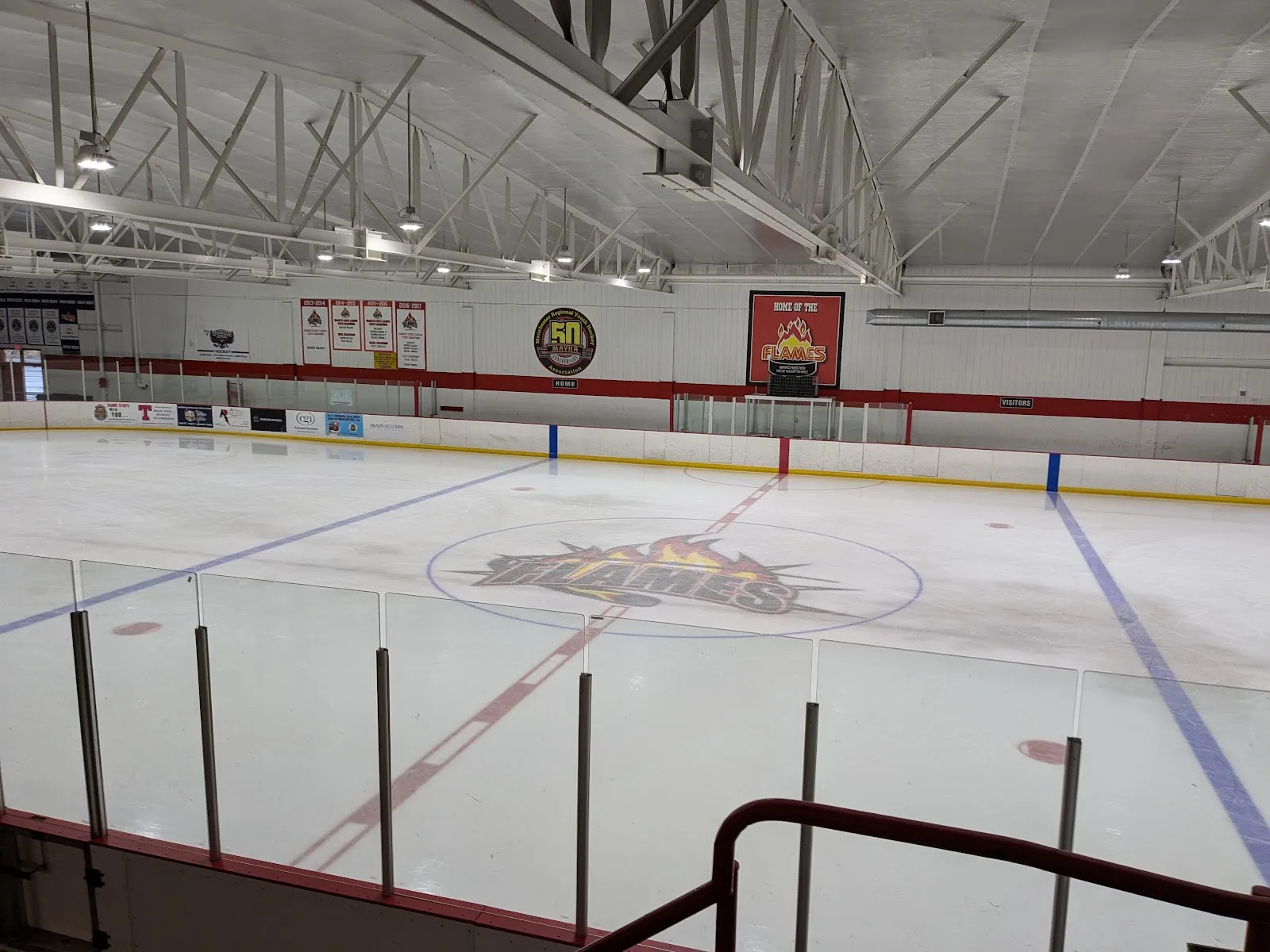 The empty ice with the centre-ice logo, seen from the stands over the glass, with banners on the far wall. — West Side Arena