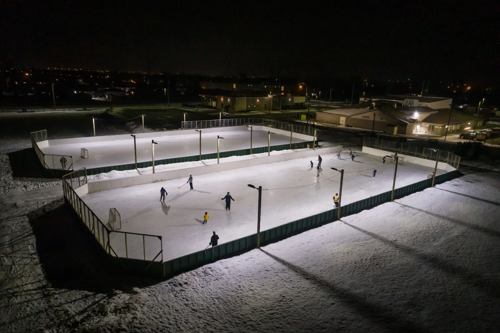 Las pistas con vallas del West Thunder Community Centre iluminadas de noche con patinadores en el hielo — West Thunder Community Centre Outdoor Rinks