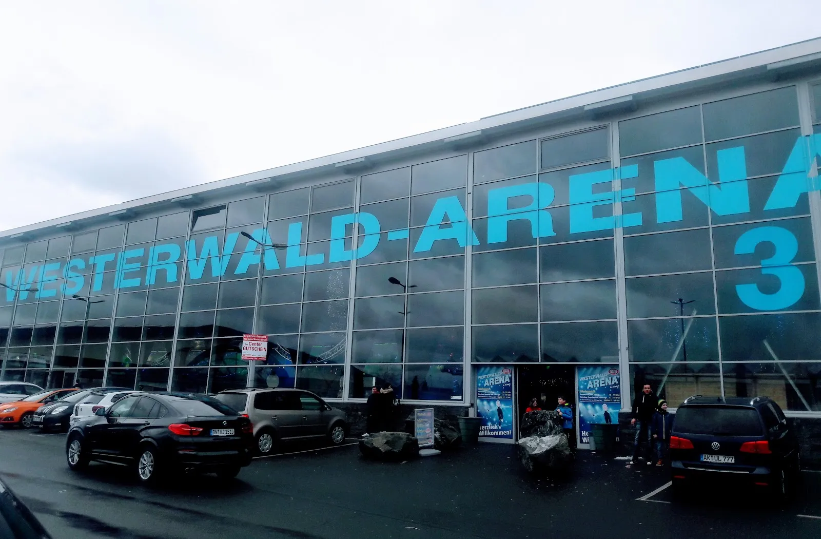 The glazed front of the arena with its large Westerwald-Arena lettering, and cars parked in the forecourt on a grey day. — Westerwald Arena Asbach (Gleit- und Rollschuhbahn)