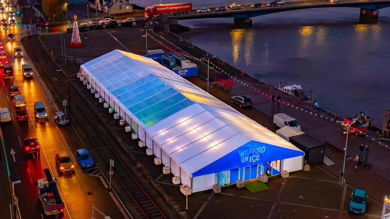 The Wexford on Ice marquee from above on Wexford Quay, lit up at dusk beside the river and the railway line — Wexford on Ice
