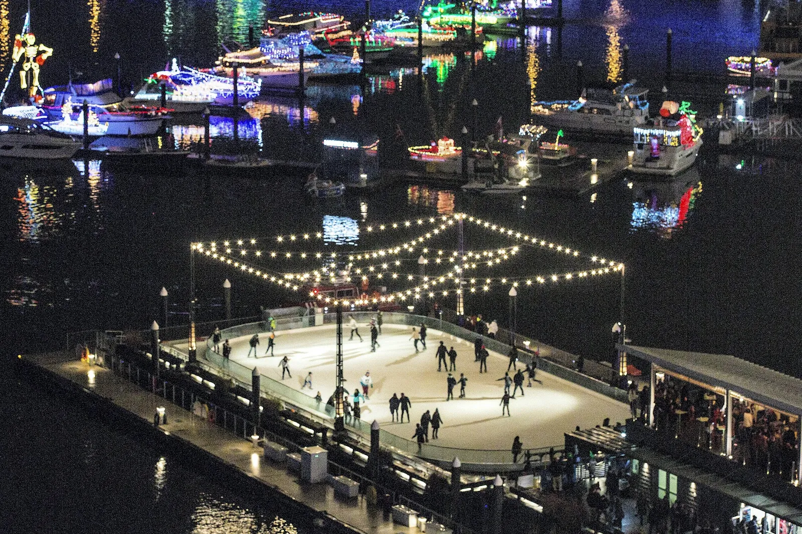 La pista flotante en el Transit Pier de noche desde arriba, con tiras de luces sobre el hielo y botes decorados en el Washington Channel. — The Wharf Ice Rink