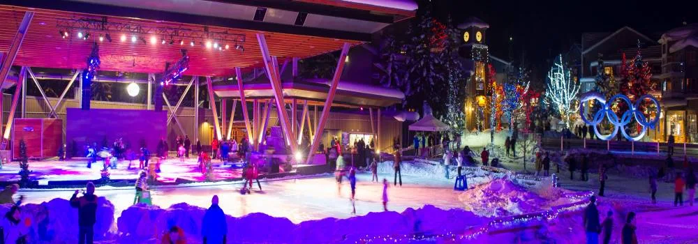 Patinadores en la pista iluminada al aire libre de la Whistler Olympic Plaza por la noche, con los aros olímpicos al fondo. — Whistler Olympic Plaza Outdoor Rink