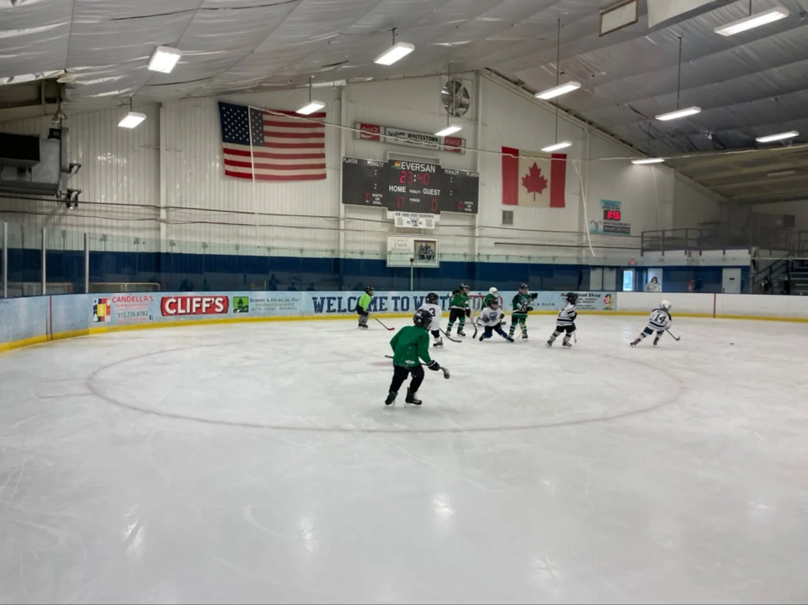 La pista de Whitestown desde el centro del hielo durante un entrenamiento juvenil, con banderas de Estados Unidos y Canadá y el marcador en la pared del fondo. — Whitestown Community Center & Ice Rink
