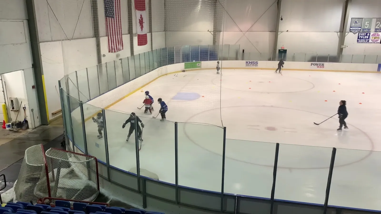 A wide view across the glass of the sheet, a few skaters spread across the ice with American and Canadian flags on the far wall. — Wichita Ice Center