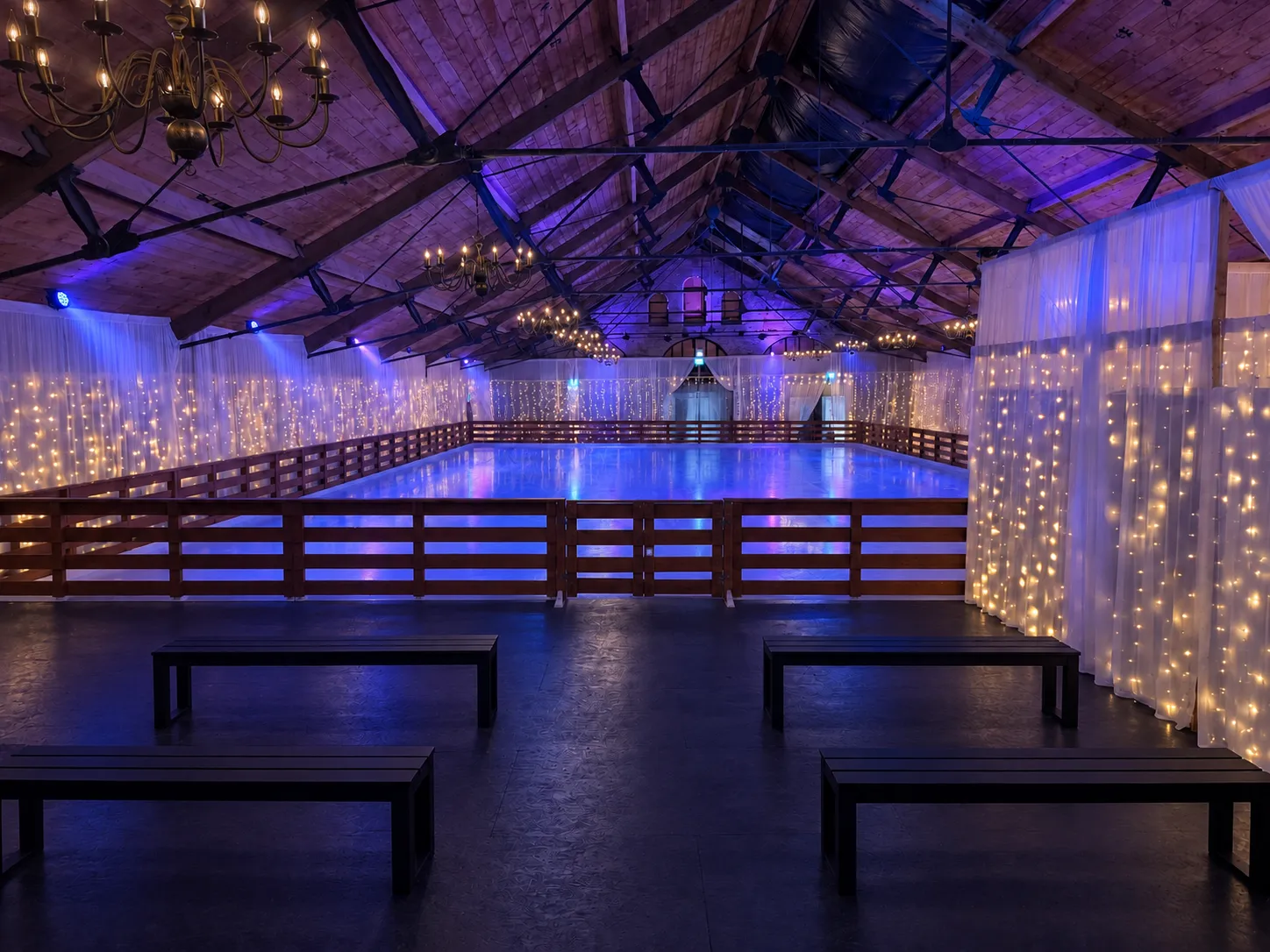 The pop-up rink inside the Great Barn, with a wooden barrier, light curtains and the timber roof trusses — Wicklow On Ice