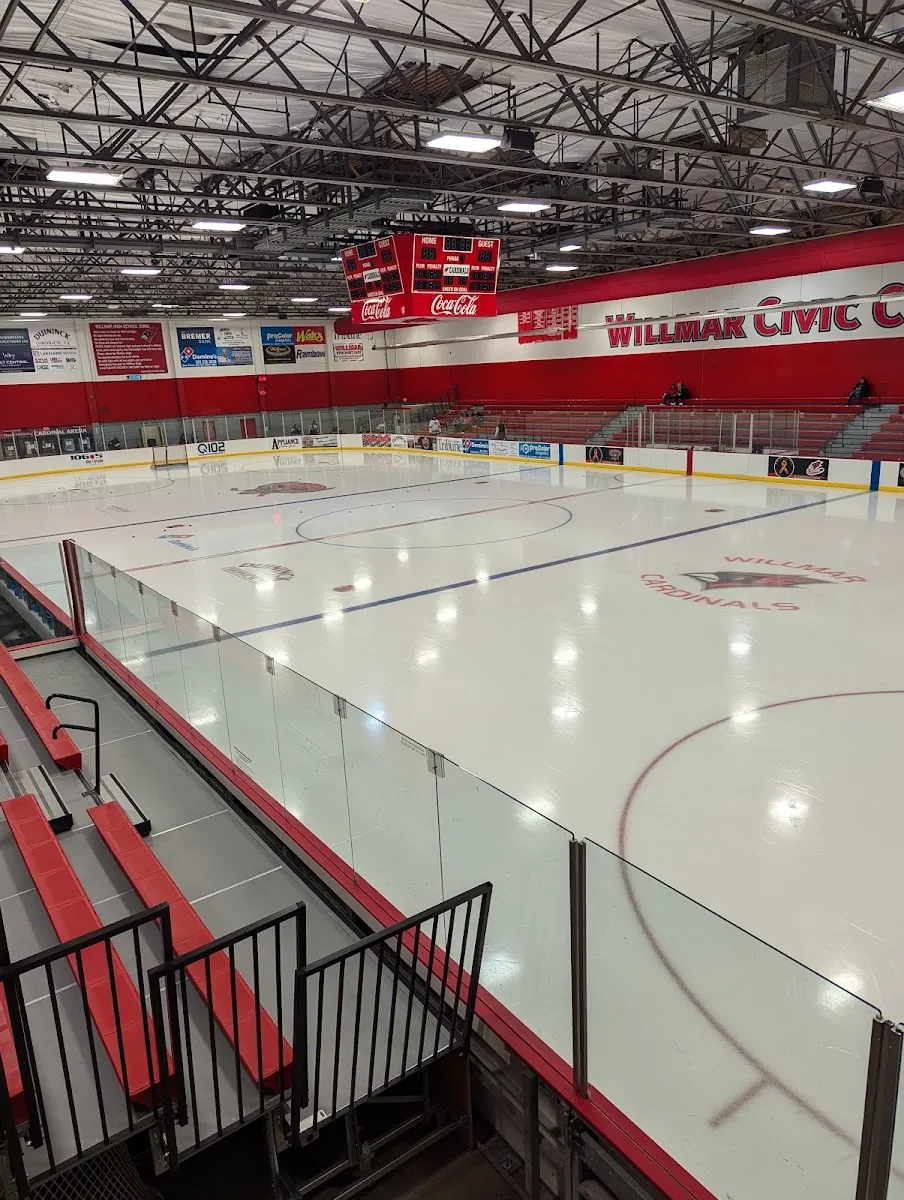 La pista principal vacía desde las gradas, con el logo de los Willmar Cardinals en el hielo, gradas rojas y las letras de Willmar Civic Center en el muro del fondo. — Willmar Civic Center