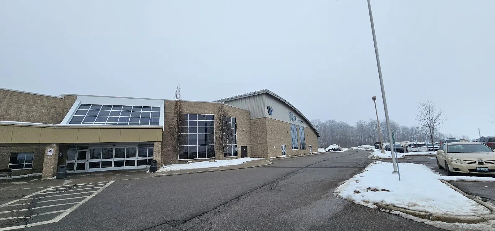 The low brick and glass front of the Wilmot Recreation Complex seen across its parking lot in winter. — Wilmot Recreation Complex (Baden)
