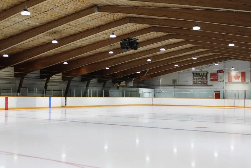 The empty ice sheet at Charles A. Barbour Arena under its exposed timber roof, with the boards and bench area at the far side — Charles A. Barbour Arena