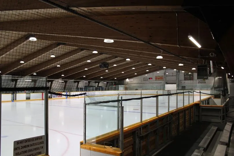 The ice at Sargent Park Arena from beside the boards, with the glass, the timber-framed roof and the bench seating — Sargent Park Arena