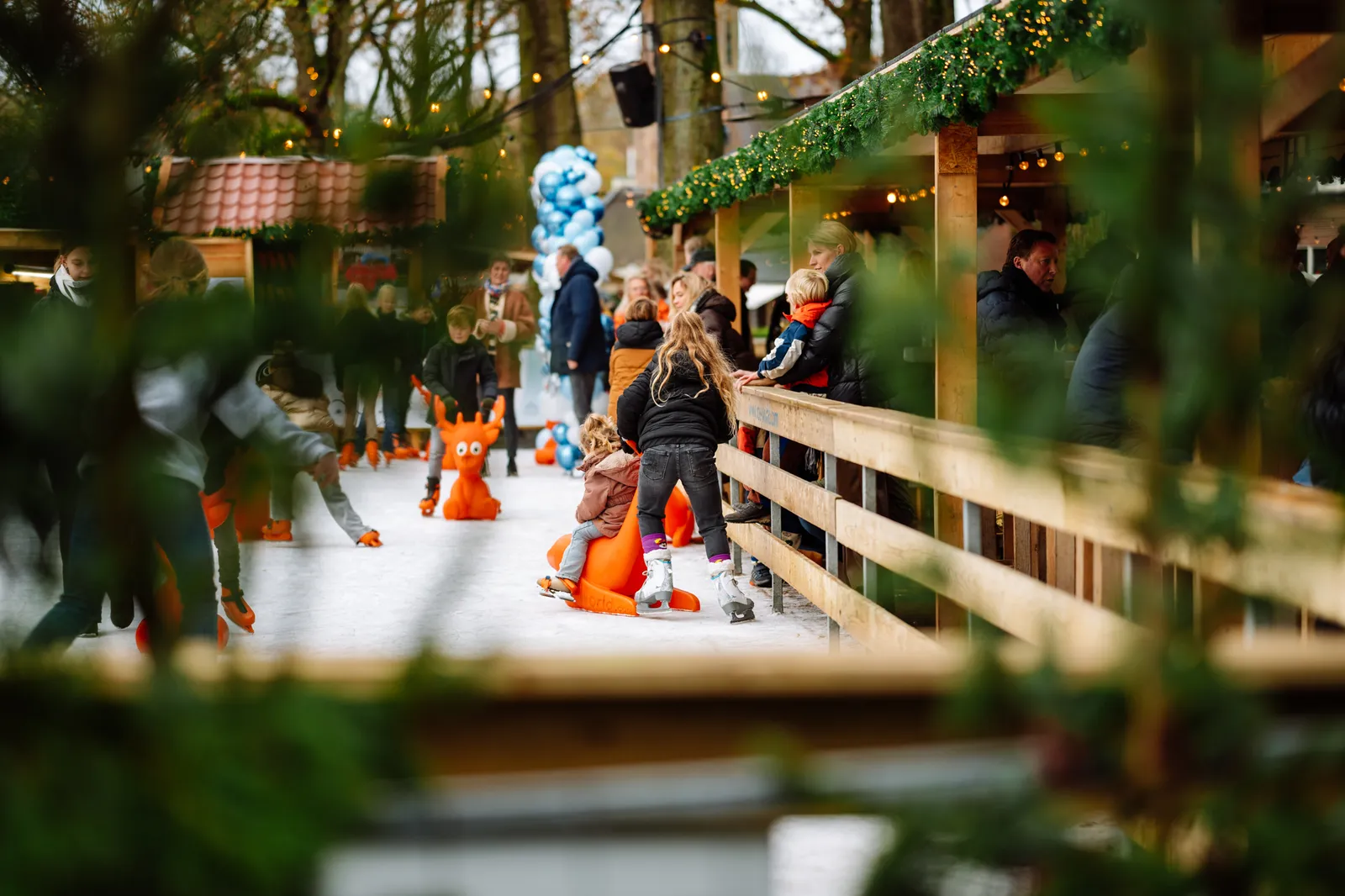 Skaters on the ice of the Winter Village Laren rink, seen between wooden fencing and festive lights. — Winter Village Laren