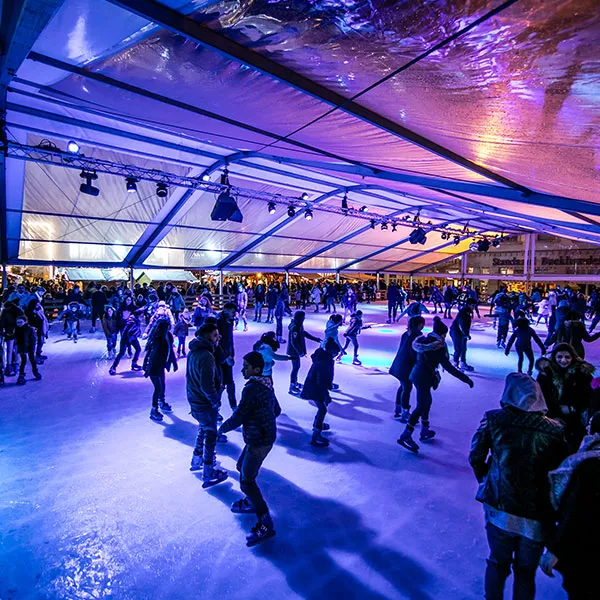 The Winter Wonders ice rink at De Brouckère in Brussels under its glass-and-canvas roof, crowded with skaters in purple and blue light. — Winter Wonders Ice Rink (Place De Brouckère)