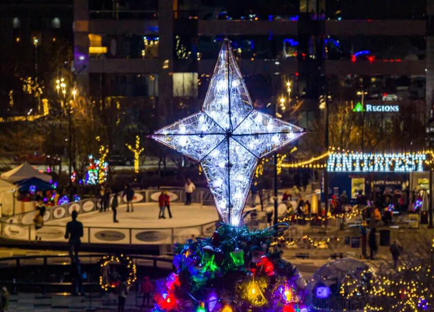 La pista al aire libre de Kiener Plaza de noche, con patinadores repartidos por el hielo junto a una estrella gigante iluminada y el letrero de Winterfest, con las torres de la ciudad detrás. — Winterfest Ice Rink at Kiener Plaza
