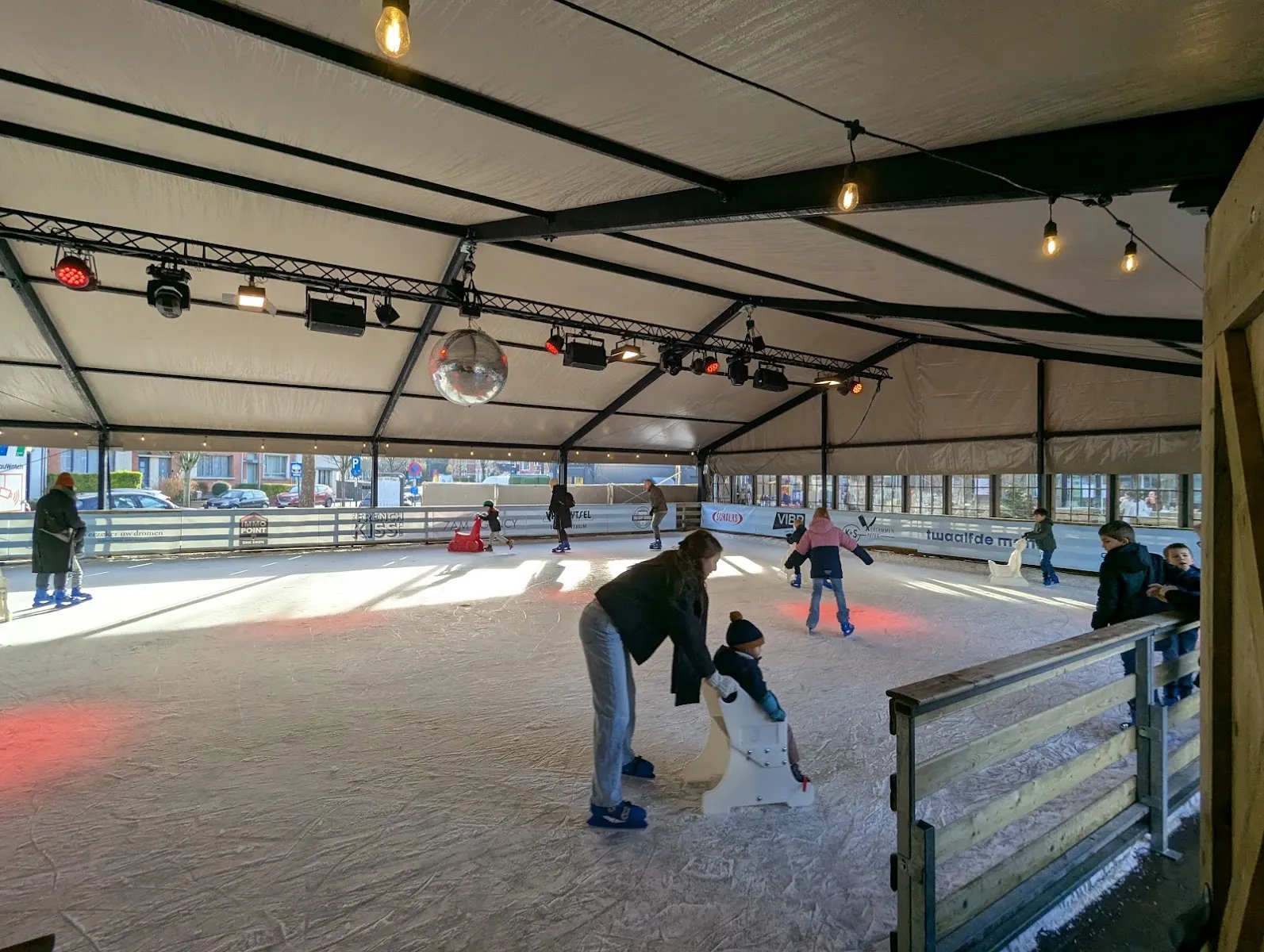 Skaters on the ice inside the Wintergem tent in Edegem, with the roof lights and the boards around the rink – Wintergem Edegem