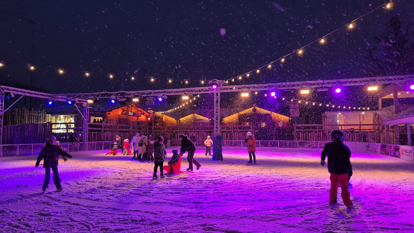 Skaters and children on the lit 900 m² ice of the Winterzauber Bazenheid village at night, under strings of lights; skaters at distance. — Winterzauber Bazenheid