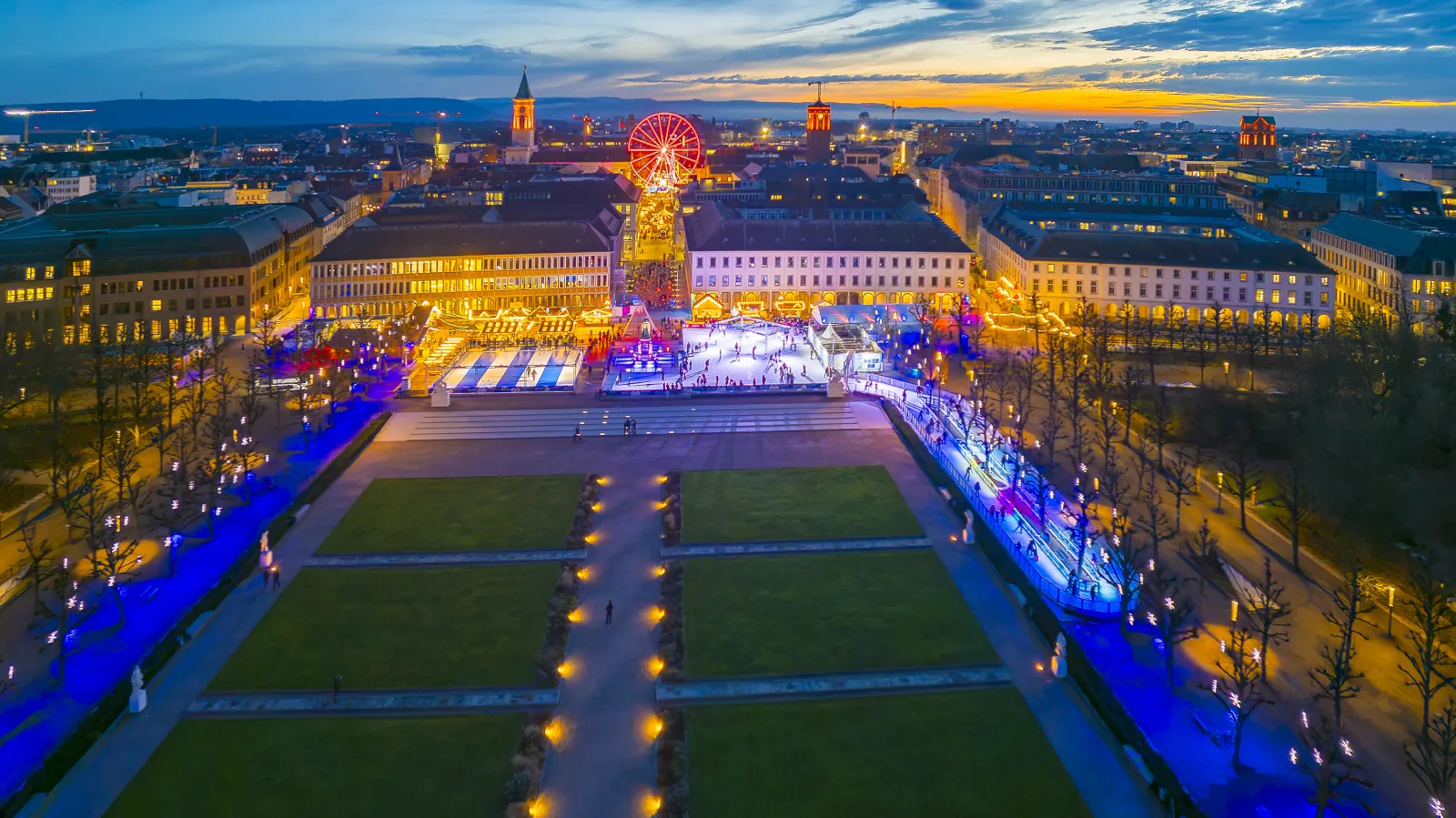 Die WINTERZEIT-Bahn und das Winterdorf auf dem Karlsruher Schlossplatz bei Dämmerung von oben gesehen – Stadtwerke Karlsruhe WINTERZEIT
