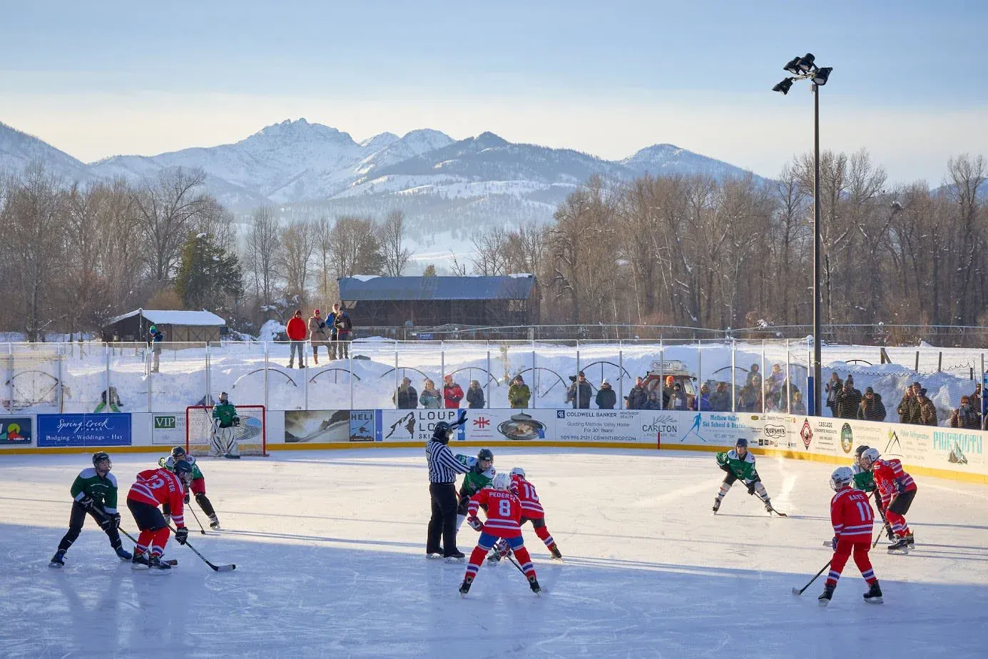 A youth hockey game on the uncovered Winthrop Rink with the snow-covered mountains behind the boards — Winthrop Rink