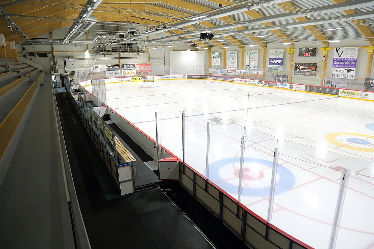 Näkymä katsomosta Kemijärven Wirta-Areenan valkoiselle jäälle, jossa on curling-ympyrät ja mainoslaidat laitojen varrella. – Jäähalli Wirta-Areena