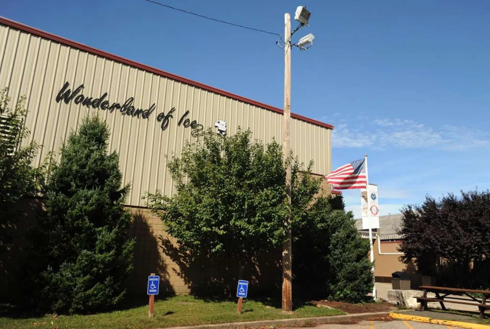 Corner of the tan metal-sided building with the 'Wonderland of Ice' script logo painted on the wall, an American flag, and accessible-parking signs out front. — Wonderland of Ice