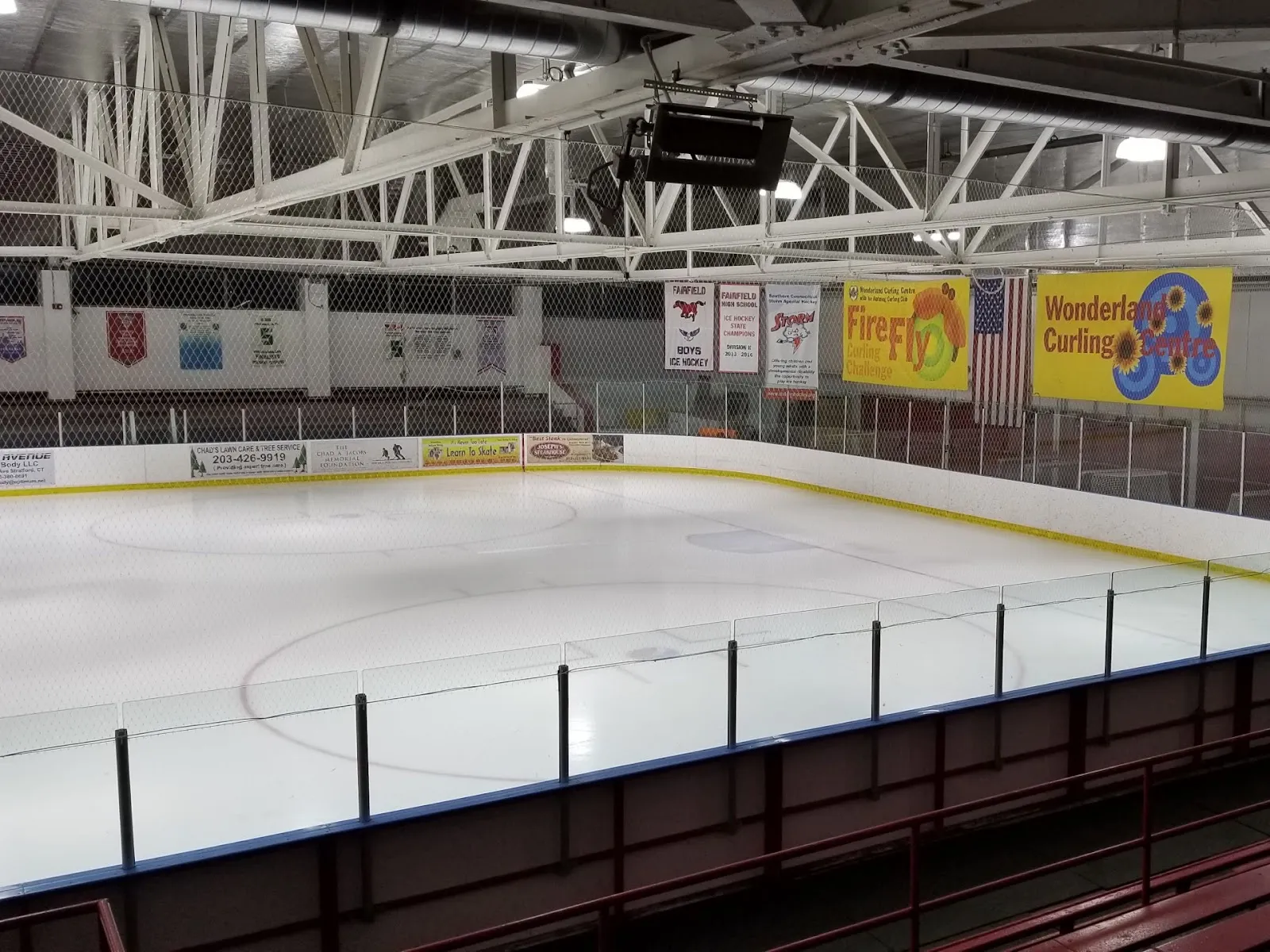 Empty ice sheet from the stands with a 'Wonderland Curling Centre' banner and Fairfield-area hockey championship banners hanging above the boards. — Wonderland of Ice
