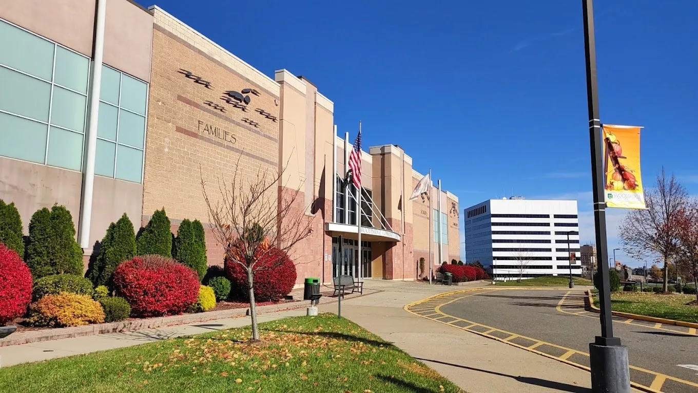 The Woodbridge Community Center's brick front with flying-figure reliefs, flagpoles at the entrance canopy and red shrubs along the walk. — Woodbridge Community Center