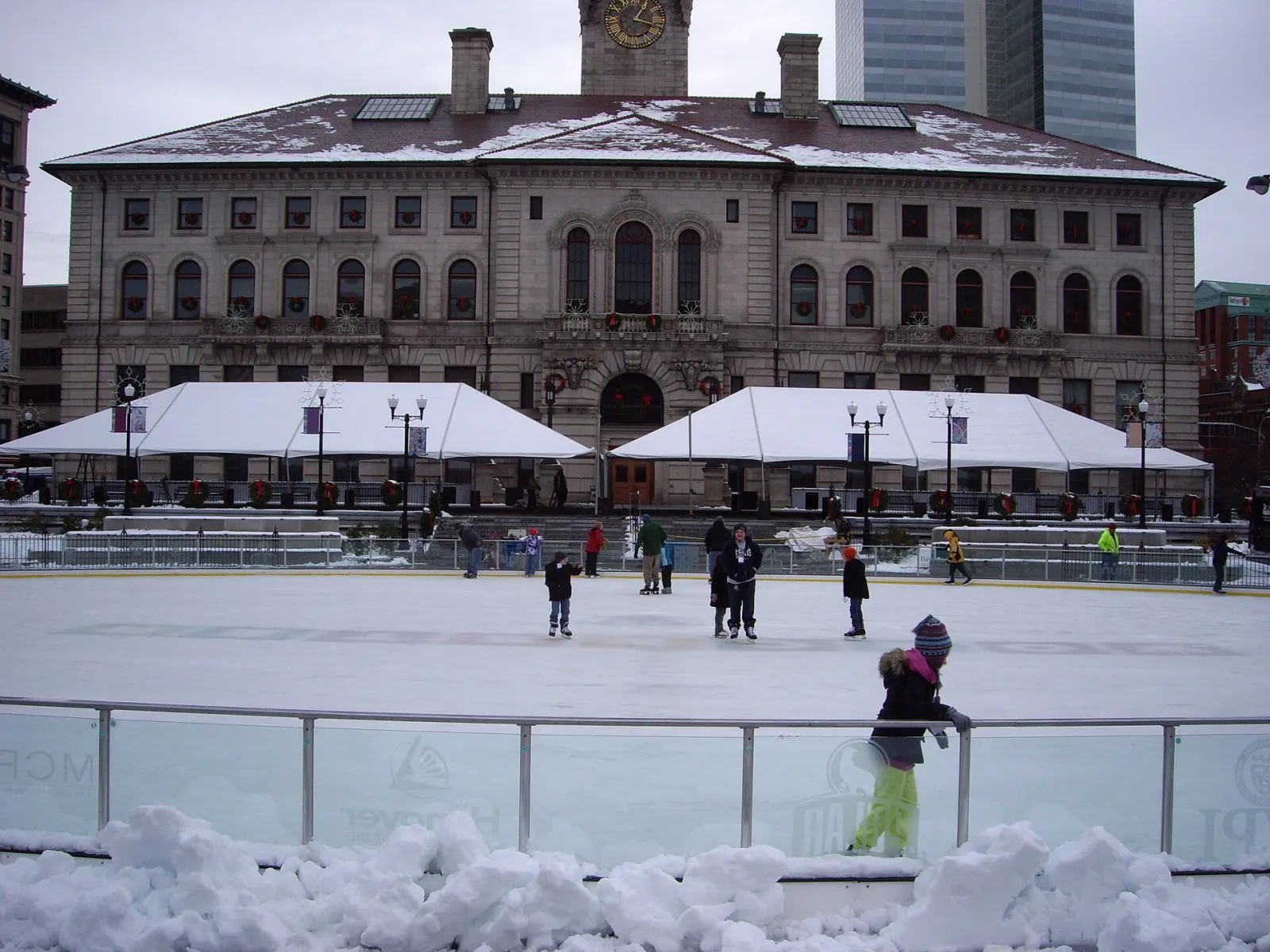 Skaters on the Common Oval ice with Worcester City Hall and the rink's white tents behind — Worcester Common Oval