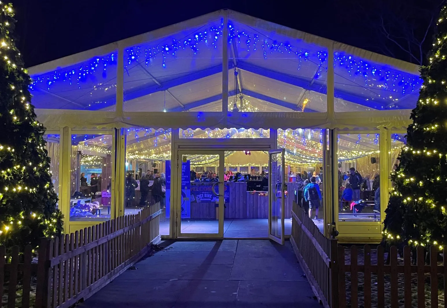 The lit marquee entrance of Worthing Ice Rink in Steyne Gardens at night, between two Christmas trees — Worthing Ice Rink