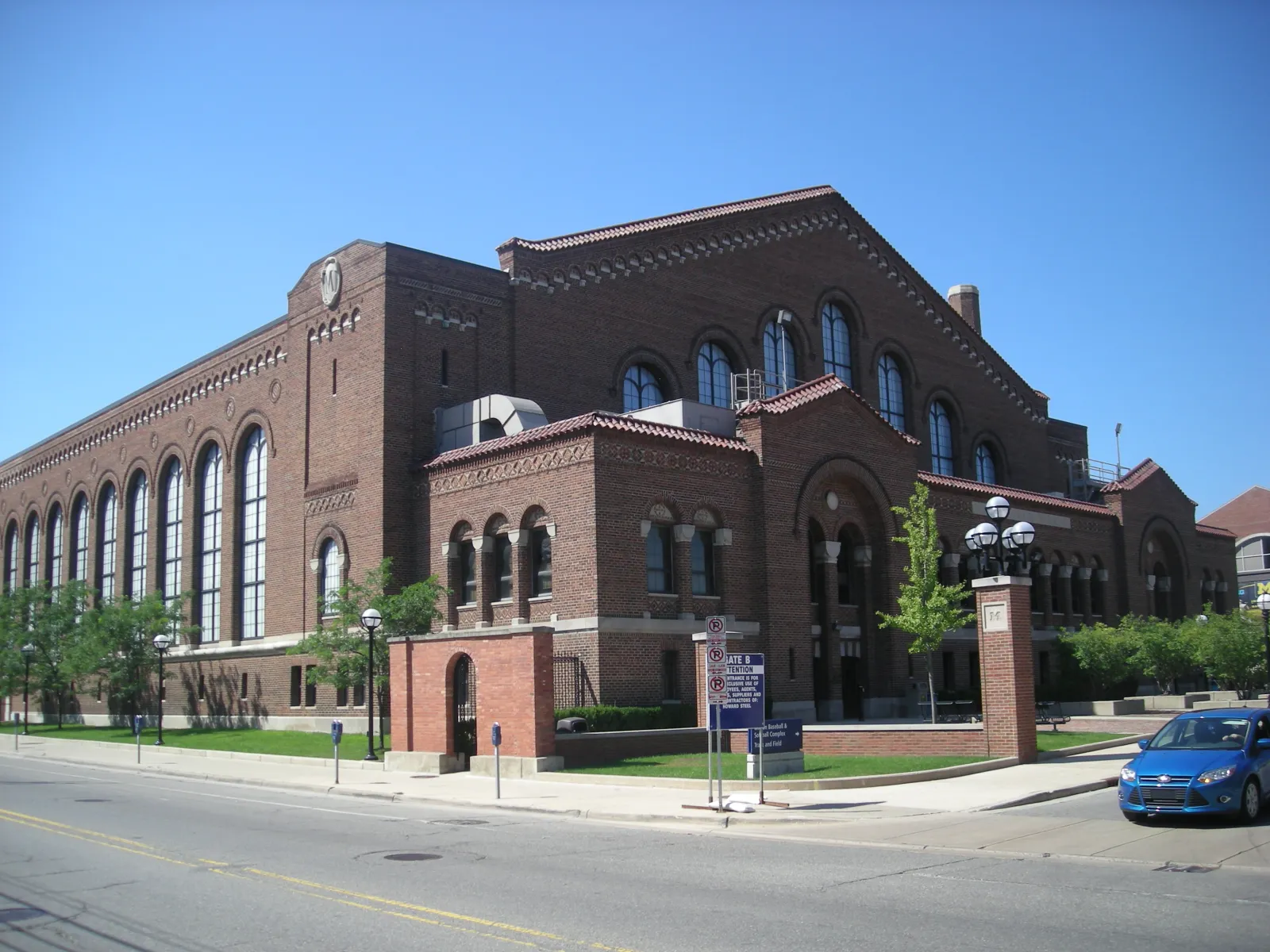 The red-brick Yost building on South State Street in sunshine, with its rows of tall arched windows, a stone-capped brick gateway and the corner entrance. — Yost Ice Arena