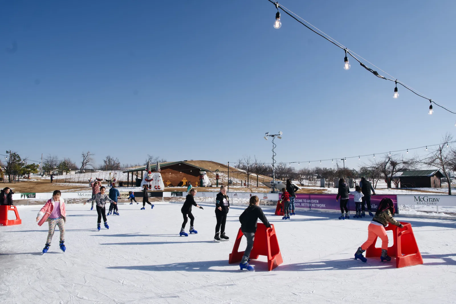 Patinadores sobre el hielo al aire libre del Yukon Ice Rink, en Chisholm Trail Park, bajo guirnaldas de luces. — Yukon Ice Rink