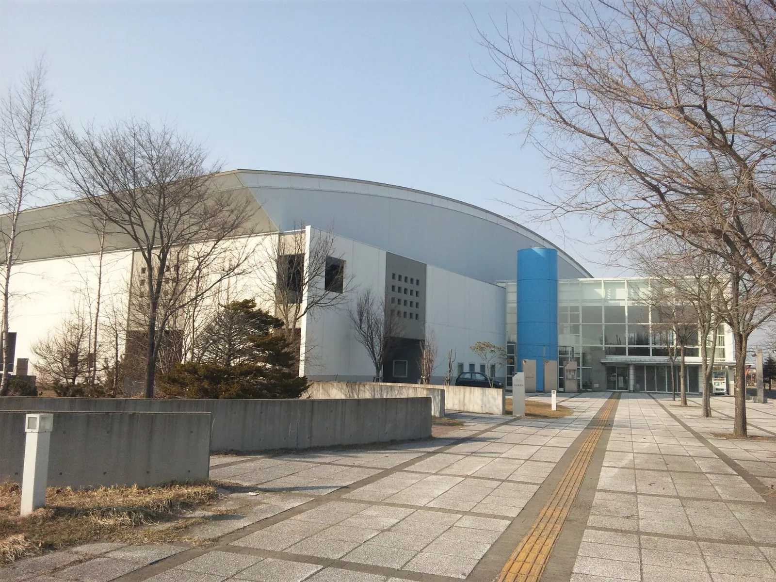 The domed Yutaka Ice Arena Kushiro (Kushiro Ice Arena) seen from the approach path, with its blue entrance tower — Yutaka Ice Arena Kushiro