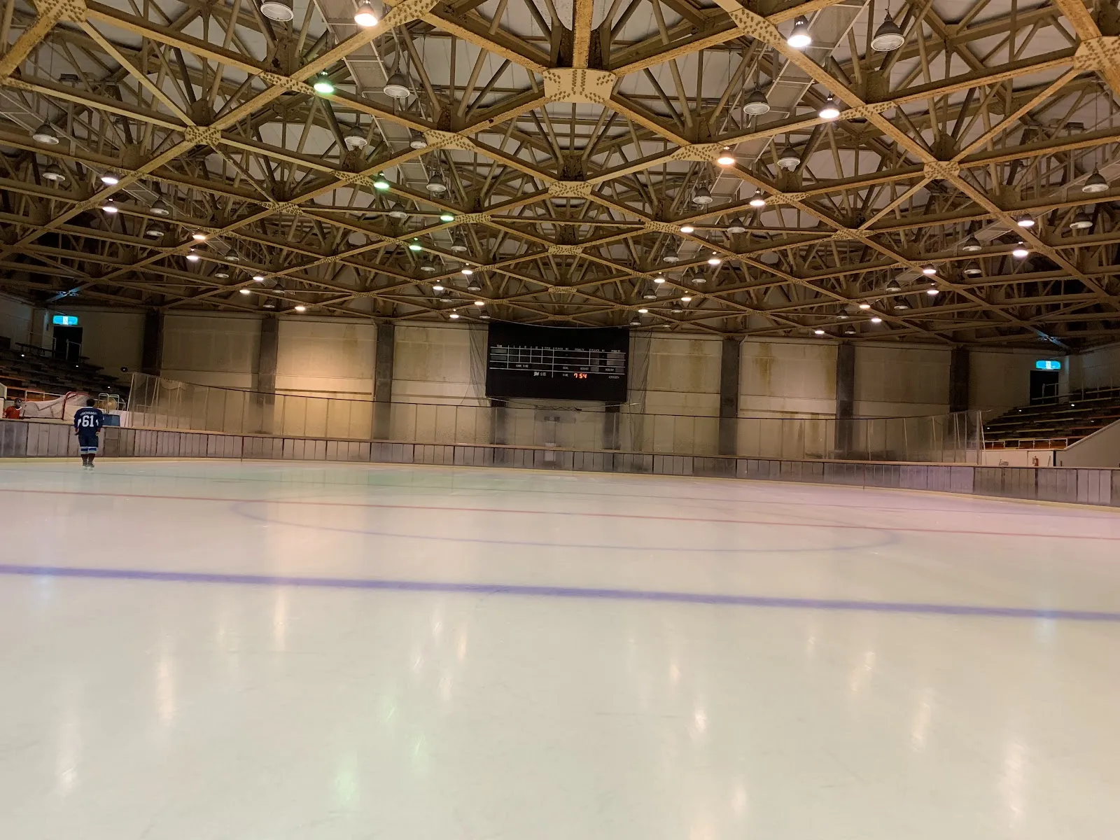 The empty ice sheet of the Yutaka Ice Arena Kushiro with its timber-lattice roof and the stands along the far side — Yutaka Ice Arena Kushiro