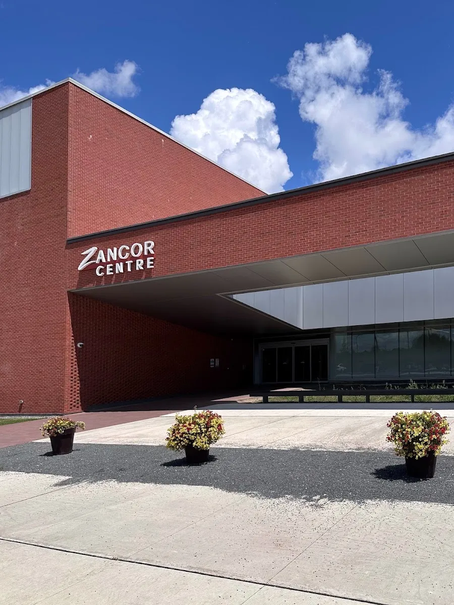 La entrada de ladrillo rojo con el letrero del Zancor Centre sobre un pasillo techado y jardineras junto a las puertas. — Zancor Centre