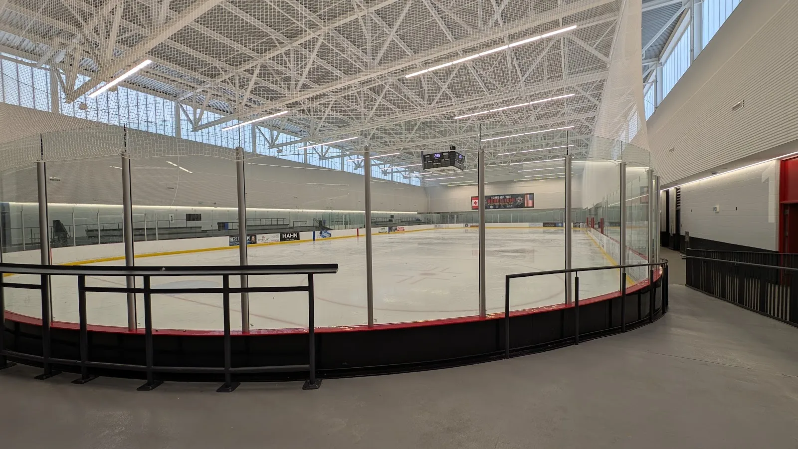 Una de las dos pistas de tamaño NHL vista desde la esquina, con un barandal de vidrio a lo largo del pasillo y un techo de armaduras de acero con tragaluces. — Zancor Centre