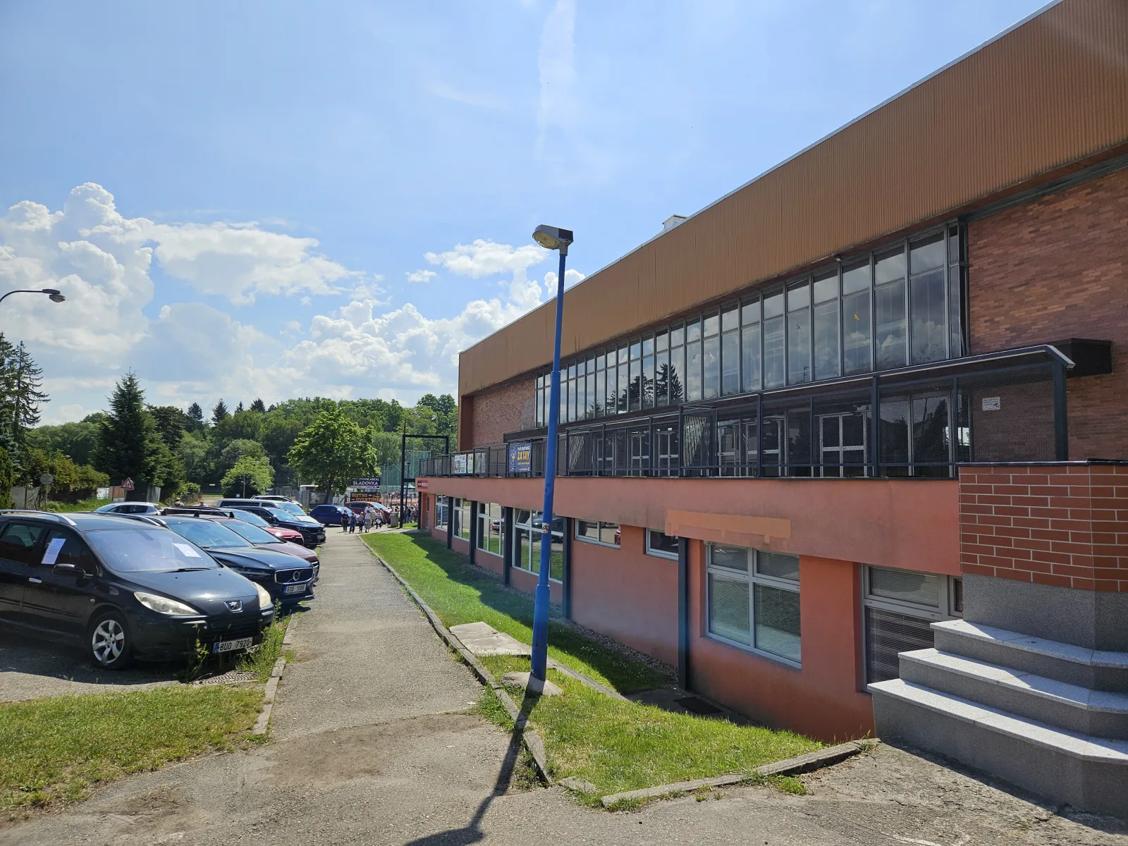 The brick and glass side of Zimní stadion Benešov, seen from the path beside the car park — Zimní stadion Benešov