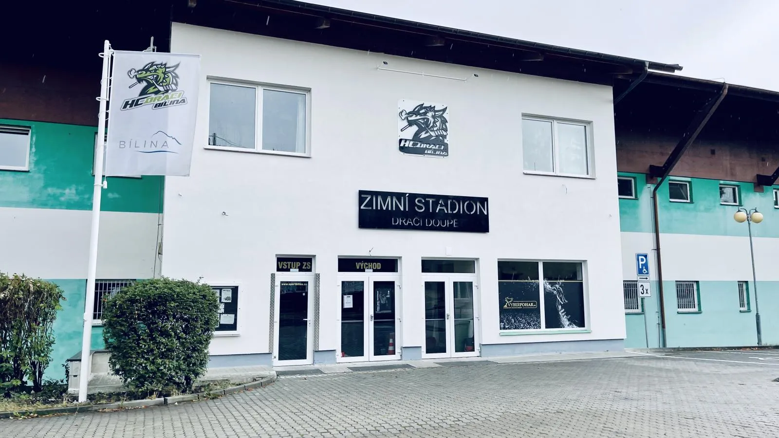 The white entrance building of Zimní stadion Bílina with the HC Draci Bílina logo and the stadium name above the doors — Zimní stadion Bílina